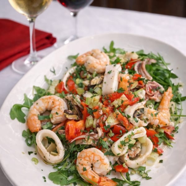 Seafood salad with shrimp, calamari, mussels, red peppers, and greens, with two glasses of wine.