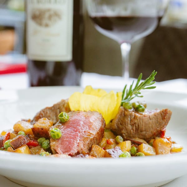 Seared steak with peas, potatoes, and rosemary, served with red wine.