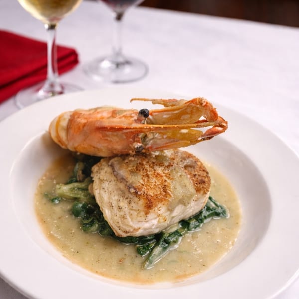 Pan-seared fish with a large prawn, spinach, and sauce, served with wine glasses.