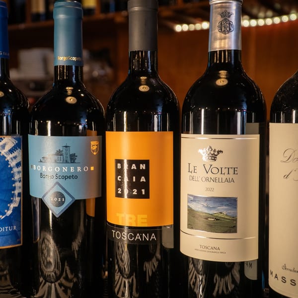 Five dark wine bottles with colorful labels, including "Borgonero" and "Le Volte," stand on a bar.