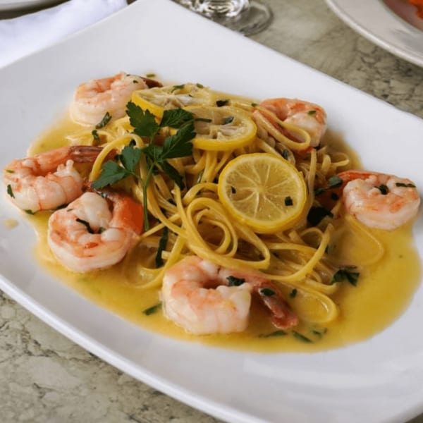 Linguine pasta with shrimp, lemon slices, and parsley in a light sauce on a white rectangular plate.